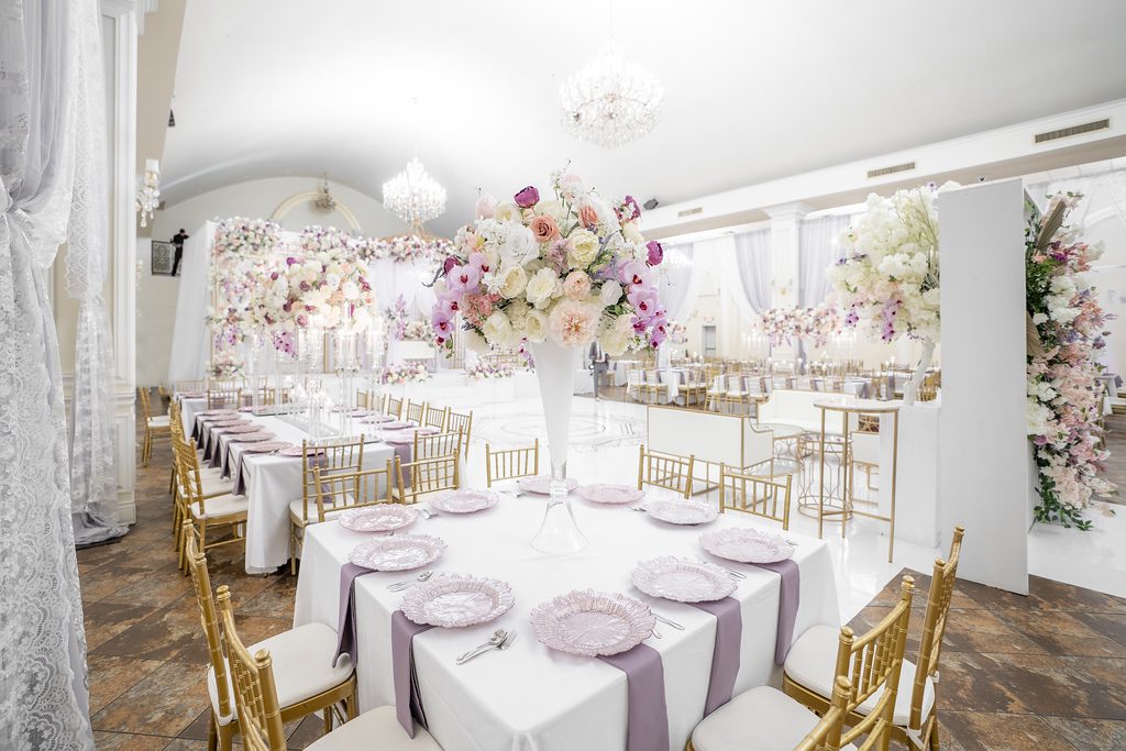 A large white table with purple napkins and gold chairs.
