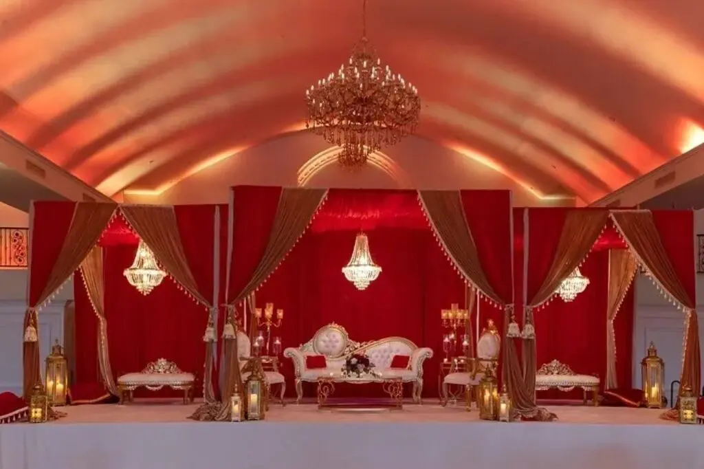 A red and gold tent with chandeliers, white furniture and curtains.